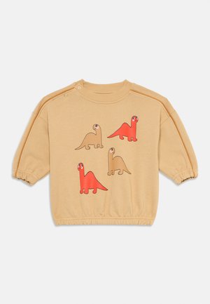 Sweatshirt beige avec quatre dinosaures de dessin animé en rouge et marron. Conçu avec des poignets élastiques et des bouton-pression sur les épaules pour un enfilage facile.