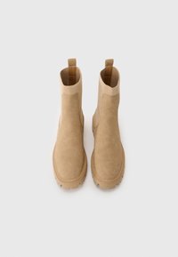 Bottines beiges à finition en suede, avec un col en tricot élastique et une semelle en caoutchouc épaisse, présentant un motif de semelle profondément embossé pour une meilleure traction.