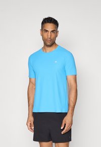 Kurzesaber T-Shirt in leuchtendem Blau, aus leichtem, glattem Stoff. Besitzt einen Rundhalsausschnitt und ein kleines Logo-Detail auf der Brust.