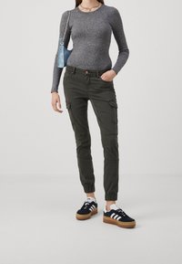 Grå ribbad långärmad topp, olivgröna cargobyxor med sidofickor och svarta sneakers med vita detaljer och gummisulor. Blå väska och smycken.