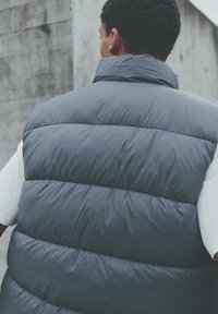 Weste in Dunkelgrau mit Steppnähten und hohem Kragen. Hergestellt aus glattem, isolierendem Material mit matter Oberfläche.