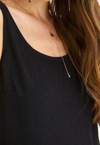 Schwarzes ärmelloses Top mit rundem Ausschnitt, glatter Textur und einer goldenen Anhängerkette mit floralem Akzent und einer langen Kette.