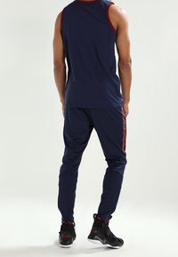 Mørkeblå atletisk tanktop med rød kant, kombineret med mørkeblå joggers med rød side-stribe, båret med sorte høje sneakers.