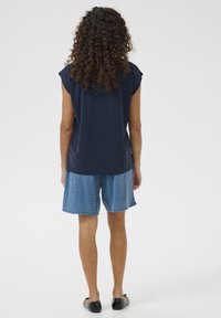 Tengerészkék, rövid ujjú felső, laza fitettel, világoskék mintás rövidnadrággal és fekete lapos cipővel párosítva, egyszerű, hétköznapi stílust mutatva.