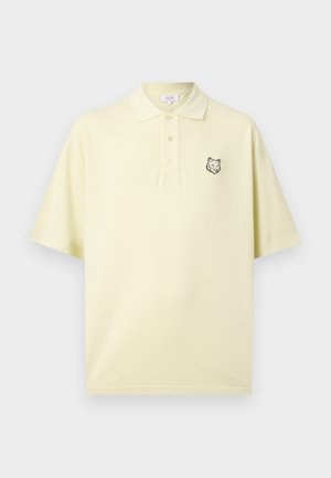 Hele kollase värvusega lühikeste varrukatega polo-särk kraega, kolmete nupuga ja väikese musta hundipea logoga vasakul rinnal.