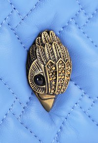 Pelle trapuntata blu con un accento in tonalità oro, caratterizzata da un design di uccello dettagliato, decorata con pietre nere e dorate.
