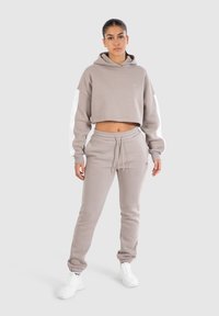 Lichtgrijze cropped hoodie met witte mouwen en een trekkoord, gecombineerd met bijpassende joggingsbroek. Beide gemaakt van zachte stof en voorzien van een logo.