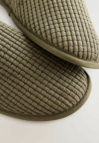 Zielone, wyściełane kapcie z tkaniny o fakturze z wzorem kratki i zaokrąglonymi krawędziami. Subtelne akcenty tekstury na całej powierzchni.