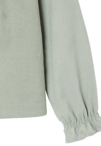 Helles grünes, geripptes Langarmkleidungsstück mit elastischen Rüschensaum, abgebildet vor einem weißen Hintergrund.