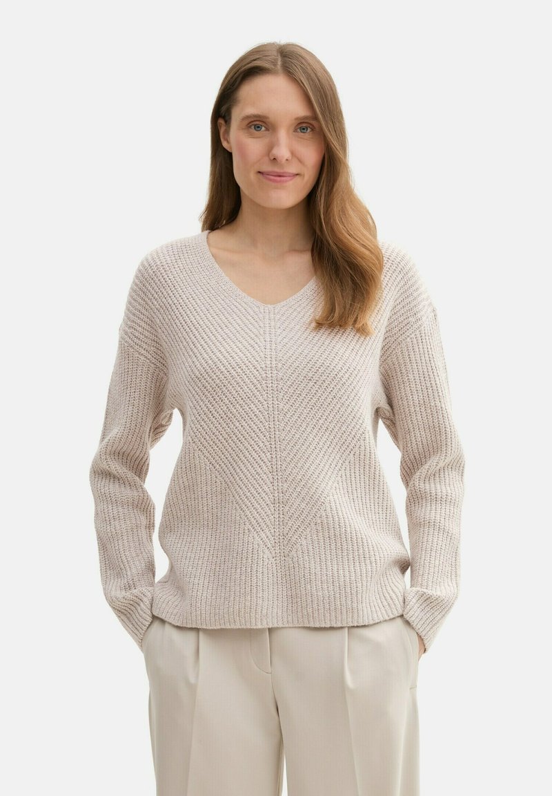 Ljus beige stickad tröja med V-ringning, med ett texturerat mönster och långa ärmar. Tillsammans med ljusa byxor.