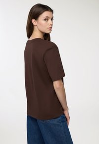 Brązowa, oversize koszulka z krótkimi rękawami, okrągłym dekoltem i gładką fakturą, zestawiona z szerokimi dżinsami. Prosty i casualowy design.