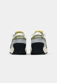 Sneakers featuring a grey and green suede upper, white accents, rubber sole with circular grips, and a logo on the heel.