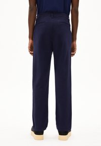 Marineblauwe wijde broek met een gladde textuur, voorzien van twee achterzakken en een hoge taille, gestyled met zwarte platform schoenen.