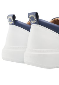 Sneakers in pelle bianca con un tab retro blu, caratterizzati da un logo nero in rilievo e suole texturizzate. Design minimalista con superfici lisce.