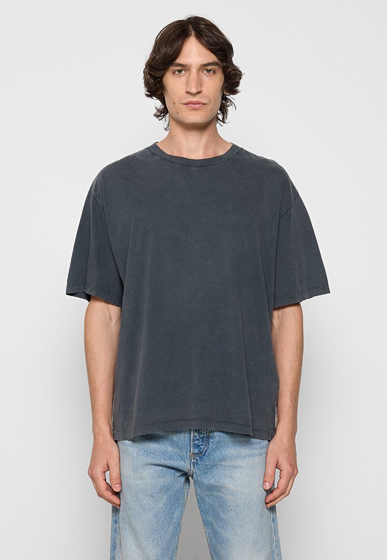 Dunkelgraues, übergroßes Baumwoll-T-Shirt mit kurzen Ärmeln, rundem Halsausschnitt und leicht strukturiertem Finish. Tragen mit hellblauen Jeans.