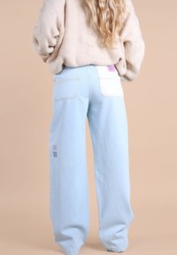 Jean large bleu clair en denim, doté de deux poches arrière, d'une étiquette blanche et d'accents brodés subtils près de l'ourlet.