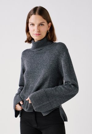 Grijze coltrui met geribbelde manchetten, ontspannen pasvorm, zijsplitten en een zachte textuur, gecombineerd met zwarte broek.