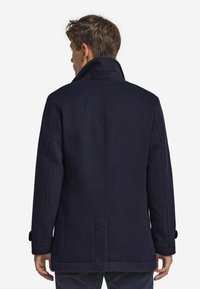 Marineblauer Wollmantel mit hohem Kragen, knöpfbaren Manschetten und strukturierter Silhouette. Verfügt über gerade Nähte und einen Rückenverschluss für Bewegungsfreiheit.