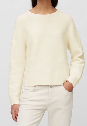 Pullover in hellcreme mit strukturiertem Strickdesign, runder Halsauschnitt, langen Ärmeln und einer cropped Passform. Kombiniert mit hellen Hosen.