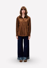 Brown suede button-up shirt with a pointed collar, paired with wide-leg dark denim jeans featuring a cuffed hem.