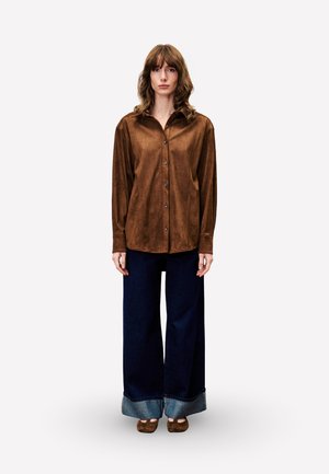 Bruine suede button-up shirt met een puntige kraag, gecombineerd met wijde, donkere spijkerbroek met een opgerolde zoom.