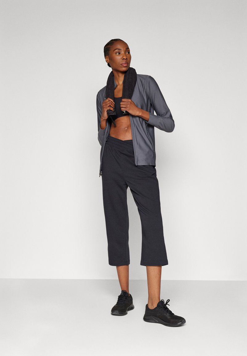 Šedá sportovní bunda na zip, černý crop top a černé zkrácené kalhoty, v kombinaci s černými teniskami; hladká textura a uvolněný střih.