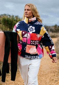 Pull en polaire avec un design en patchwork coloré dans des tons de bleu, rose et jaune. Dispose d'un col montant et d'une fermeture éclair. Texture douce.