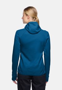 Felpa blu con design aderente, dotata di cappuccio con coulisse, maniche lunghe e tessuto liscio e strutturato. Le cuciture visibili aggiungono dettagli.