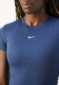 Nærbilde av en person som har på seg en tettsittende marineblå Nike-trøye med en hvit Nike swoosh-logo på brystet, som viser nakke og del av ansiktet.