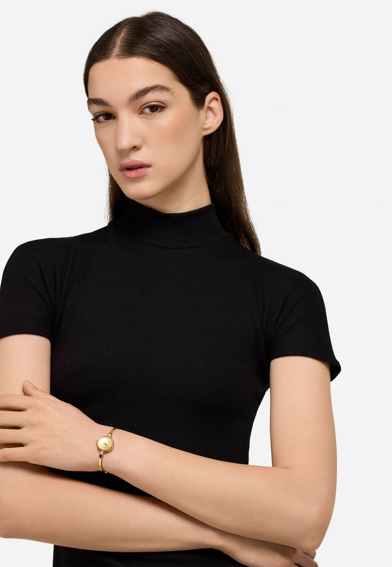 Czarny, dopasowany top z krótkim rękawem i wysokim kołnierzem, w zestawie ze złotą bransoletką z okrągłym akcentem. Gładka tekstura i bezszwowy design.