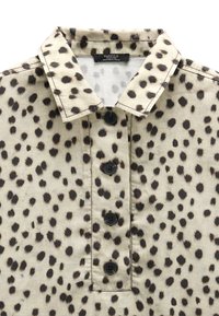 Beżowa koszula w czarne nieregularne plamy w kolorze pantery, z wyprofilowanym kołnierzykiem i czterema czarnymi guzikami z przodu.