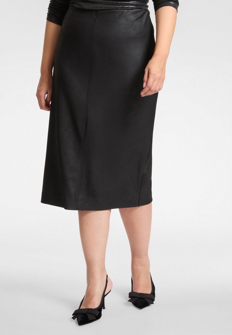 Czarna skórzana spódnica midi o gładkiej fakturze, prostym kroju i detalach z przeszyciami. W zestawieniu z czarnymi sandałkami na obcasie z paskiem na piętę i ozdobą w postaci kokardki.