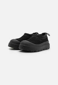 Black casual shoes with a chunky sole, featuring a mix of smooth and textured materials, a rounded toe, and elasticized collar for easy wear.