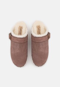 Braune Wildleder-Clogs mit einem weichen, cremigen Fellfutter, verstellbarem Riemen und dezentem Branding auf der Innensohle. Robuste Gummisohle.