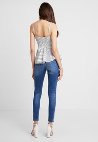 Bílý a černý pruhovaný top s peplum střihem a tenkými ramínky, spárovaný s modrými úzkými džíny a bílými sandály na vysokém podpatku. Hladká látka a přiléhavý design.