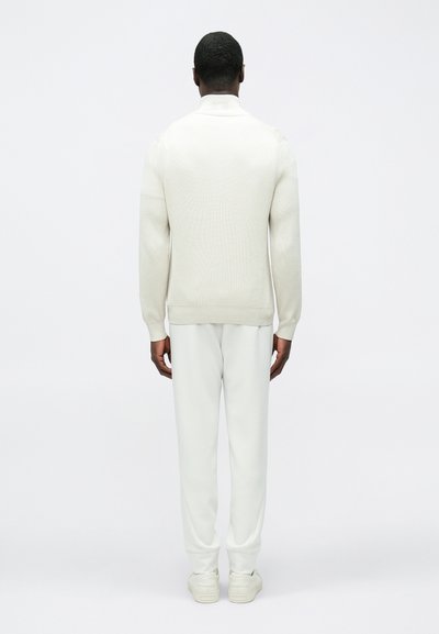 Pull blanc à côtes avec col montant, assorti à un pantalon de survêtement léger et des baskets blanches, vu de dos.