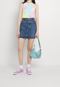 Top s ramínky v pastelových barvách s technikou tie-dye, denimová mini sukně, růžové tenisky s bílou podrážkou a tyrkysová kabelka s řetízkovým akcentem.