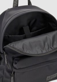 Zaino nero con un esterno in tessuto morbido, dotato di un compartimento principale con zip, tasca frontale e logo del marchio sulla parte anteriore.