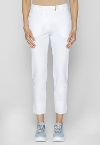 Białe, dopasowane spodnie z przodu z kieszeniami oraz złotym detalem zamka, w komplecie z jasnoniebieskimi trampkami z dekoracyjnymi akcentami.