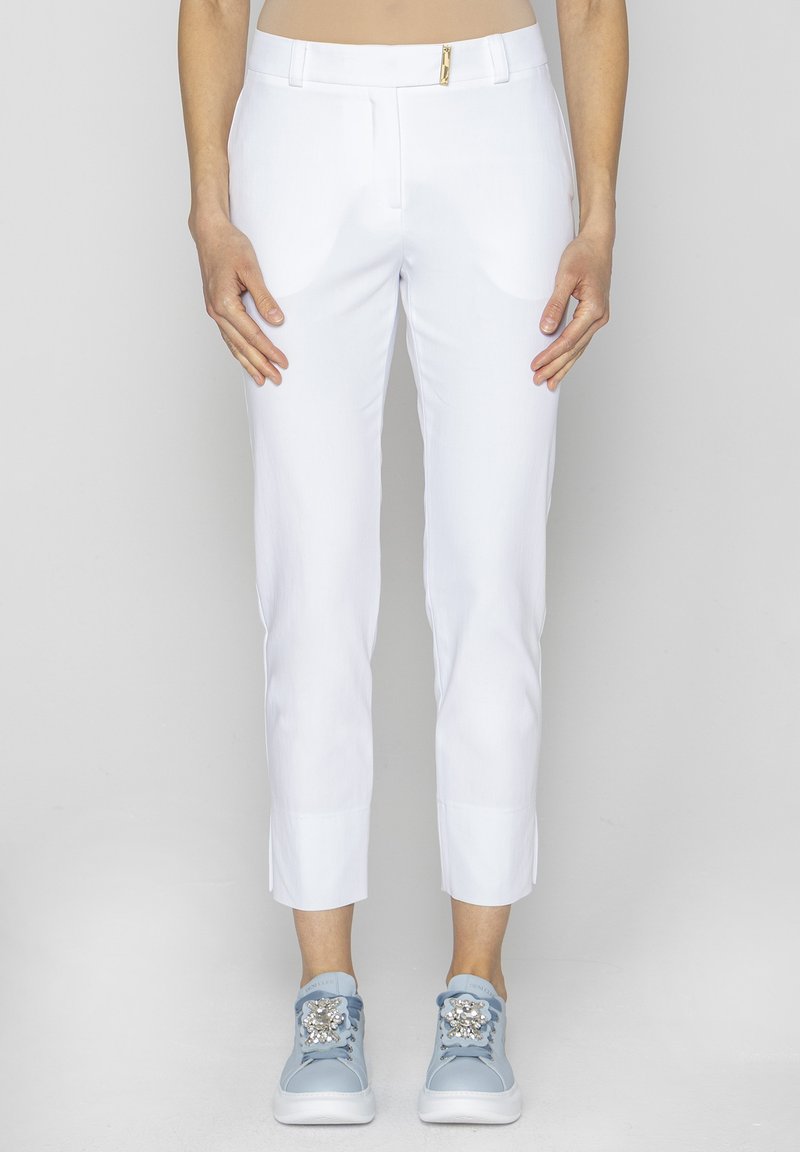 Białe, dopasowane spodnie z przodu z kieszeniami oraz złotym detalem zamka, w komplecie z jasnoniebieskimi trampkami z dekoracyjnymi akcentami.