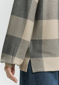Beige en grijs geblokte gebreide trui met brede mouwen, zijsplitten en een zachte textuur. Heeft diagonale en horizontale streepjespatronen.