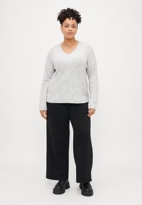 Suéter de malha com gola em V de manga longa, cinza claro, combinado com calças largas pretas e botins pretos.