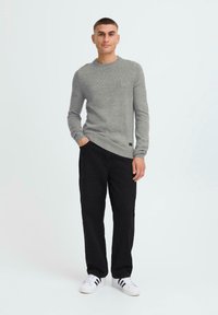 Gray knitted sweater, round neckline, long sleeves; paired with black pants and white sneakers. Simple design, soft texture, no patterns.