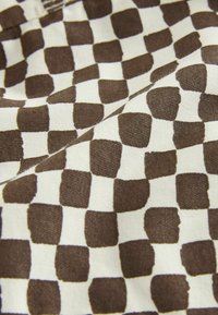 Tkanina s nepravilnim uzorkom šahovnice u smeđoj i bijeloj boji, prikazuje teksturu i nabore materijala.