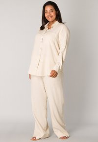 Light beige linen shirt with a collar and front pocket, paired with matching loose-fitting trousers. Smooth texture, casual fit.