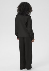 Schwarzes Langarmshirt mit dekorativen Spitzenakzenten an den Ärmeln, kombiniert mit locker sitzenden schwarzen Hosen, glatte Textur und entspannte Silhouette.