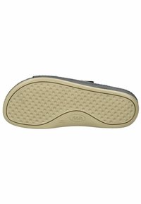 Semelle de chaussure noire avec une surface texturée comportant des creux circulaires pour une meilleure adhérence. Matériau en caoutchouc beige. Logo de la marque visible au centre.