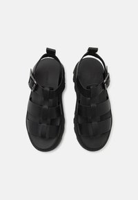 Black sandals with a woven design, featuring a buckle strap and textured sole. Made of synthetic material for durability and comfort.