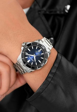 Edelstahl-Uhr mit blauem Zifferblatt, silbernen Akzenten und Datumsfenster. Verfügt über ein Edelstahlarmband und eine Lünette im Taucherstil.