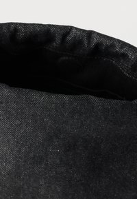 Κοντινό πλάνο της μαύρης εσωτερικής επένδυσης και της υφής υφάσματος μιας τσάντας ή θήκης από σκούρο τζιν, με ανοιχτό άνοιγμα, σε απλό φόντο.